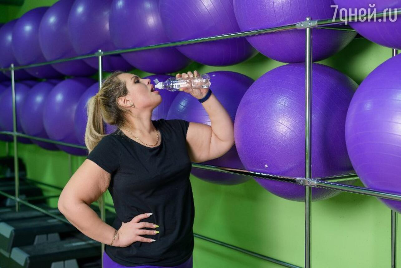 Женщина с лишним весом пьет воду на тренировке